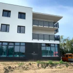 Nowoczesny budynek usługowo-mieszkalny z dużymi witrynami na parterze, balkonami na wyższych kondygnacjach oraz kontrastową elewacją w nowoczesnym standardzie